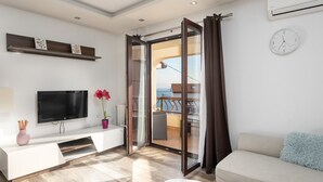 A modern living room with a flat-screen TV, a white sofa, a coffee table, and a sliding glass door leading to a balcony. - Apartment Melani (Kvarner - Mošćenička Draga) (Mošćenička Draga)