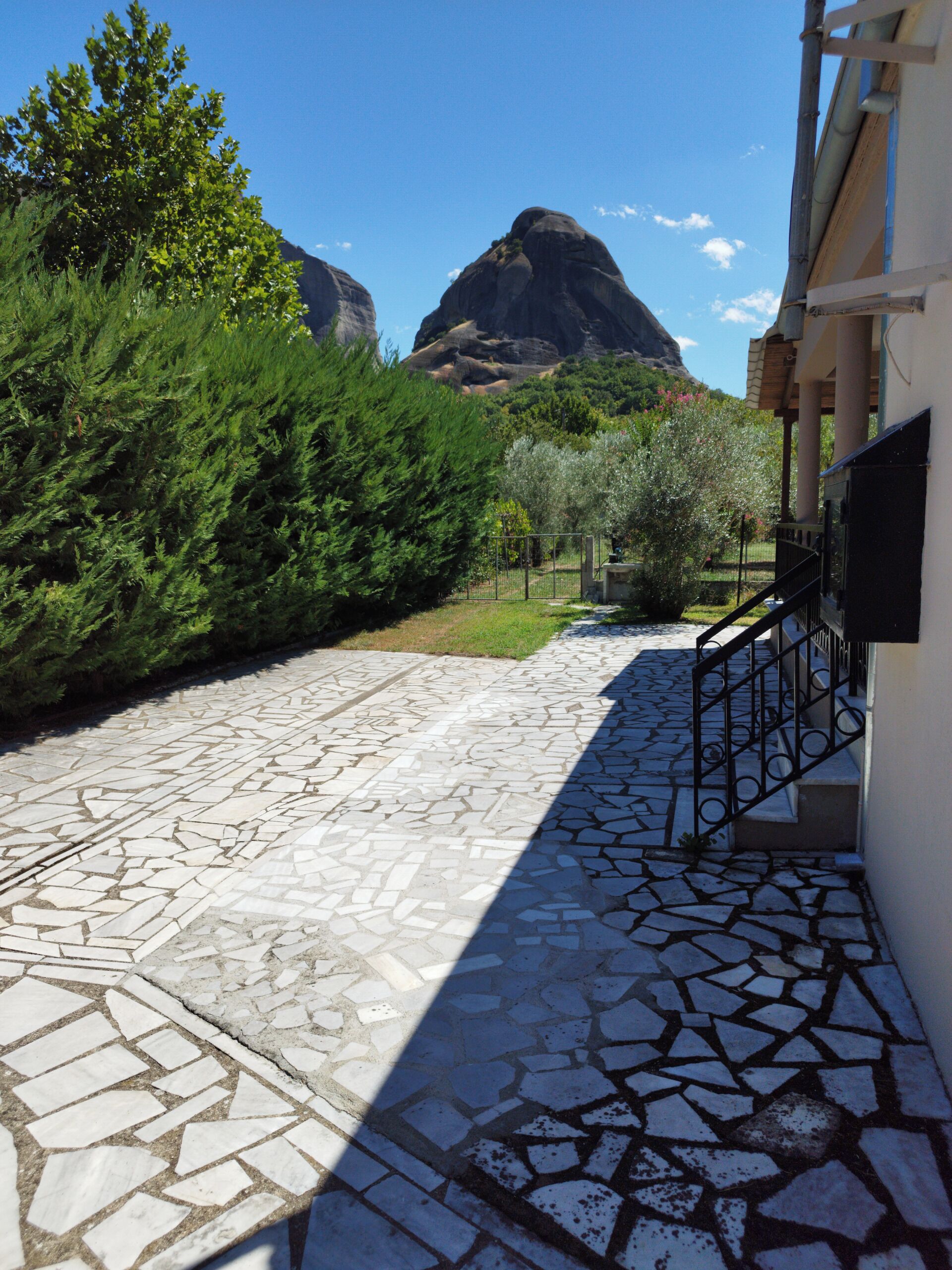 A stone-paved pathway leading to a building with a metal railing and a view of a mountain.