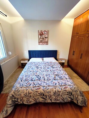 A bedroom with a bed, wooden wardrobe, and a wall-mounted artwork. - Kastraki House with a view (Kastraki)