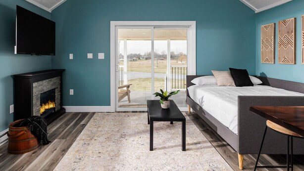 A bedroom with a bed, a TV, a fireplace, and a view through a sliding glass door. - River & Charm: 2 Homes, on 10 Acres Near Clayton (Clayton)