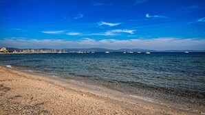 A beach with clear water, boats, and distant mountains.
