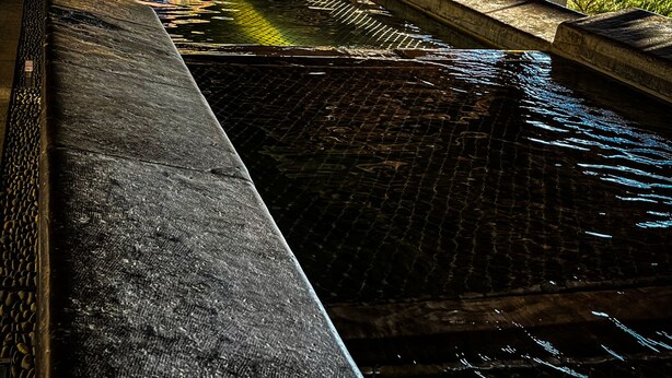A covered swimming pool with a stone edge and a metal railing.