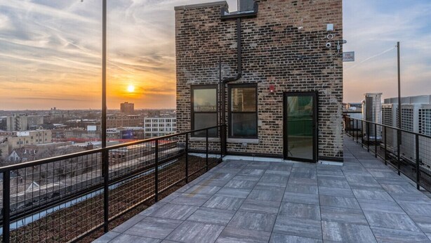 Una terraza en la azotea con pared de ladrillo, ventanas amplias y barandilla de metal.