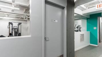 Een moderne kantoorruimte met een witte deur, een zichtbaar vluchtteken en een blik op een sportschoolgedeelte op de achtergrond.