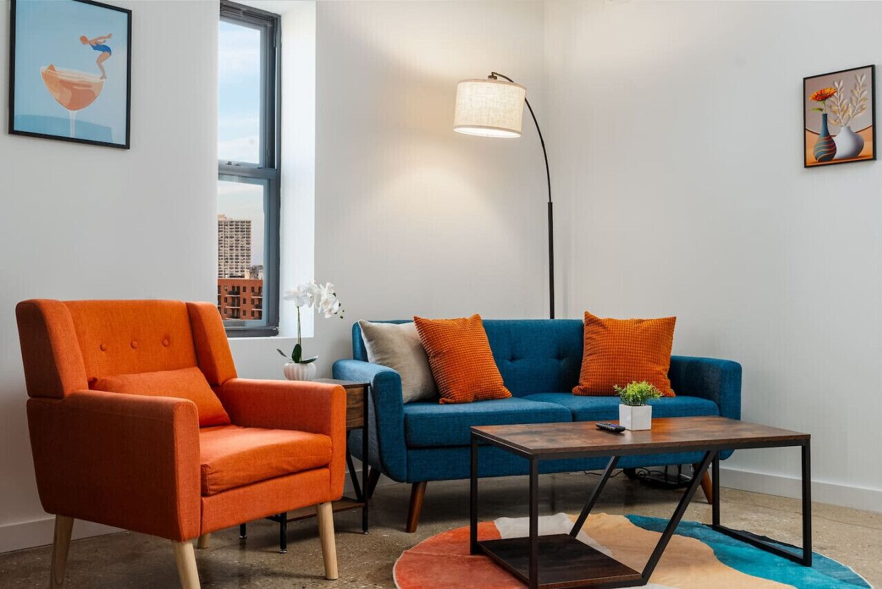 A modern living room with a blue sofa, orange armchair, and a floor lamp.