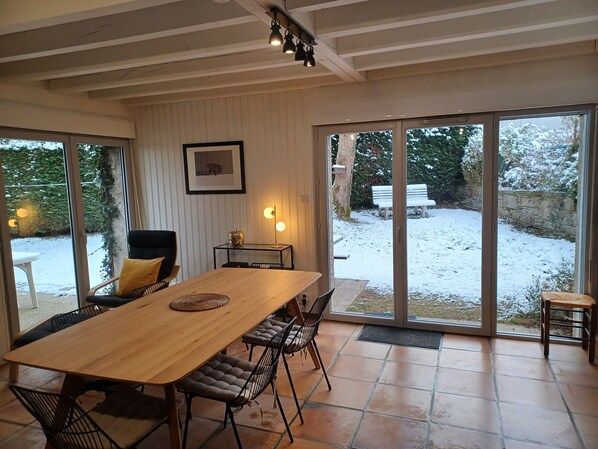 Ein Essbereich mit einem Holztisch und Stühlen, einem gerahmten Bild an der Wand und Blick auf einen verschneiten Garten durch große Schiebeglasfenster.