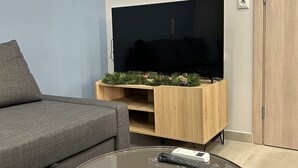 Un salón con un sofá gris, un mueble de madera para el equipo de entretenimiento con un televisor, y una mesa de centro de vidrio con un control remoto.
