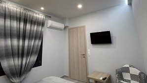 Un dormitorio moderno con una cama, una mesita, una silla, un televisor y un aire acondicionado.