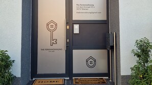 Een moderne hotelentree met een donkere deur, een glasraam erboven en een welkomstmat.