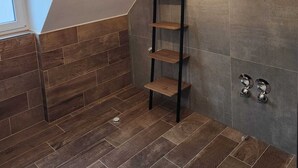 Een moderne kamer met een schuin dak, een houten vloer, een geometrische hanglamp, een ladderplank en een wandrek voor handdoeken.