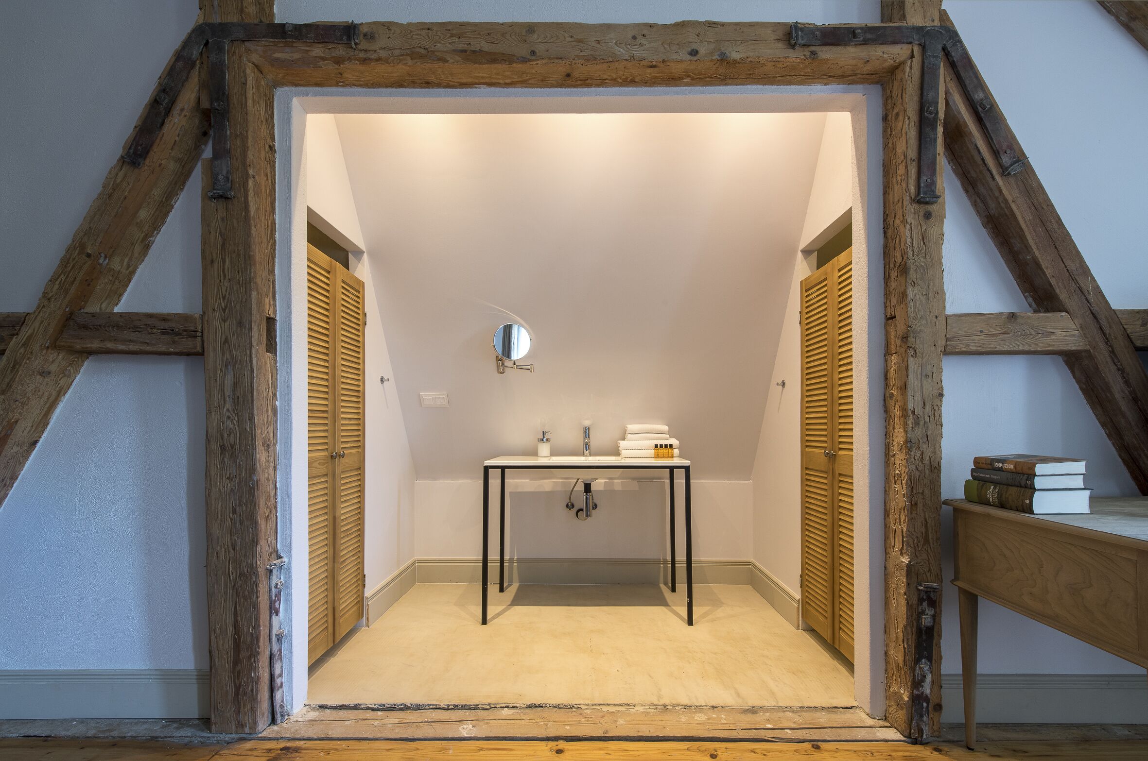 A small, well-lit room with a wooden ceiling, a table with toiletries, and a mirror.
