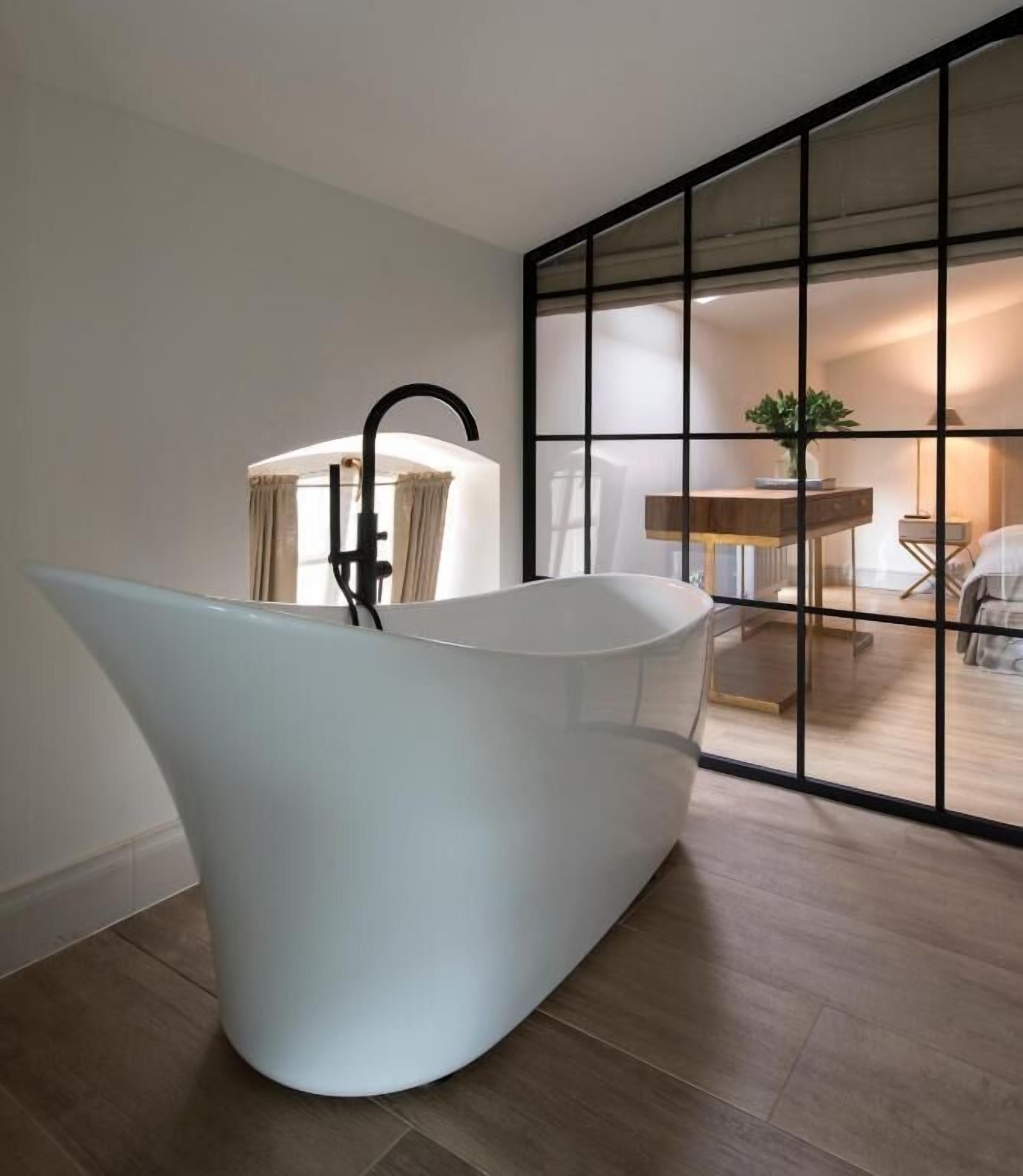 A modern bathroom with a freestanding bathtub, a black faucet, and a large window with a view of a dining area.