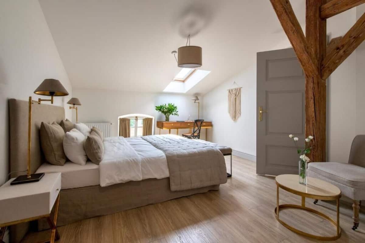 Et soveværelse med seng, natbord, lampe og et rundt bord med en vase.