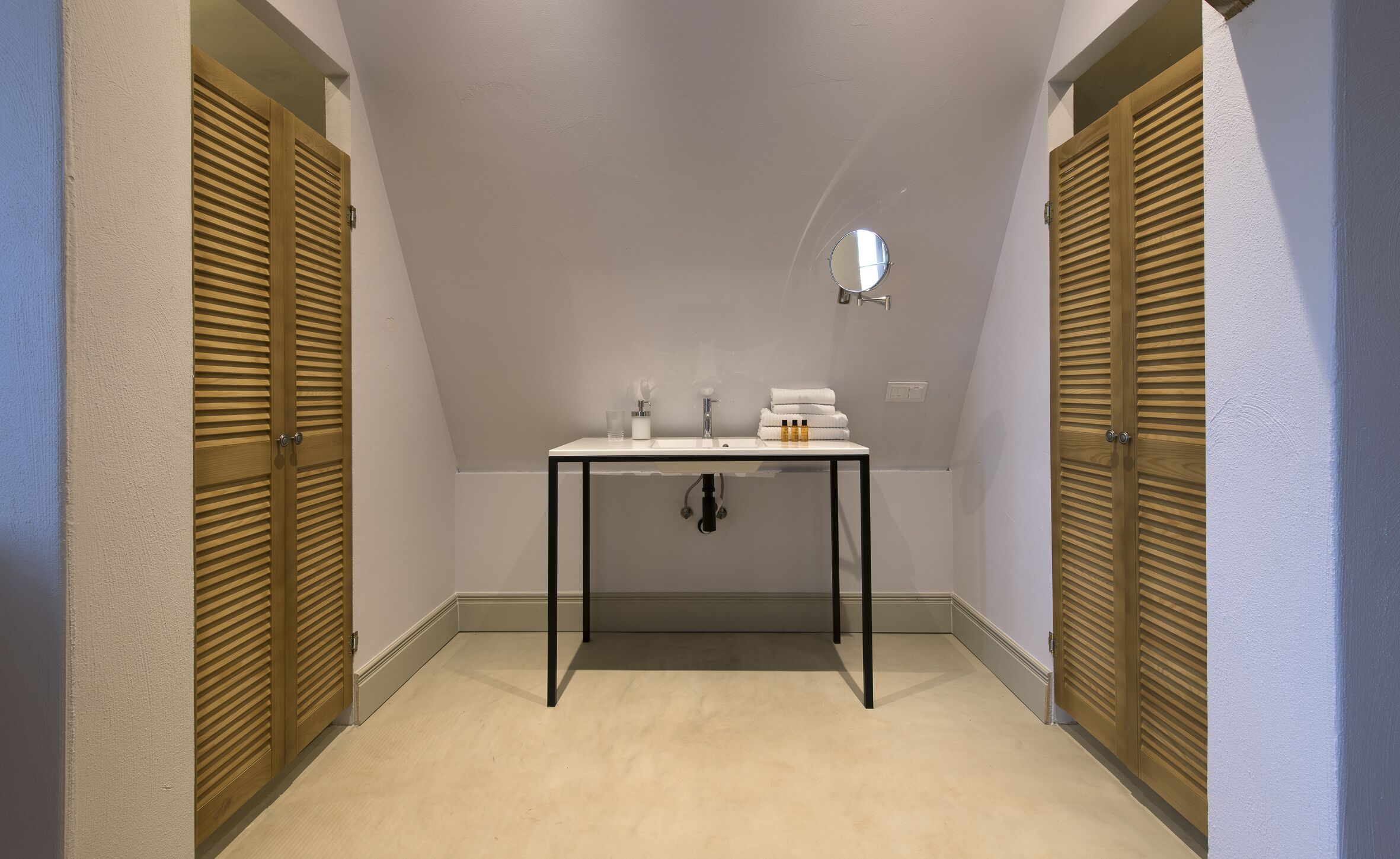 Un pasillo estrecho con un lavabo blanco, espejo y artículos de aseo.