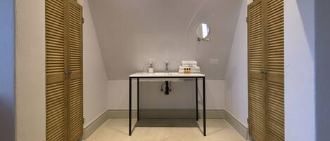 Un pasillo estrecho con un lavabo blanco, espejo y artículos de aseo.