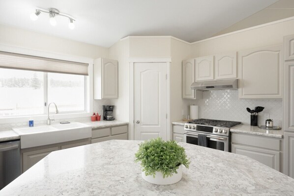 Una cocina moderna con armarios blancos, encimera de granito, estufa integrada y ventana con persianas.