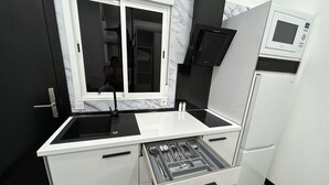 Una cocina compacta con microondas integrado, un lavamanos y un cajón con utensilios.