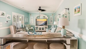 A living room with a TV, a decorative word 'Sea' on the coffee table, a ceiling fan, and a large window. - Ocean Lakes Site MH191A with Lake View, 4-bedroom 3-bath with loft. Sleeps 10 (Myrtle Beach)