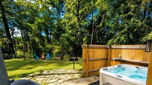 Un bain à remous avec un revêtement de sol en pierre, une terrasse en bois et une cour arrière clôturée, aménagée avec des sièges d’extérieur.