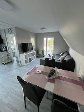 Ein modernes Wohnzimmer mit Essbereich, einem Flachbildfernseher und einer Couch mit Kissen.