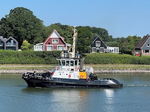 Ein Schlepper auf einem ruhigen Fluss, im Hintergrund Häuser und Grünpflanzen.