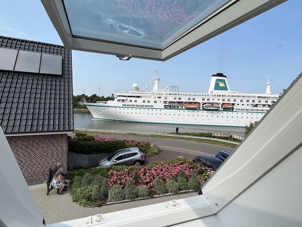 Ein Blick auf einen Fluss, im Hintergrund ein großes Kreuzfahrtschiff namens 'DEUTSCHLAND'.