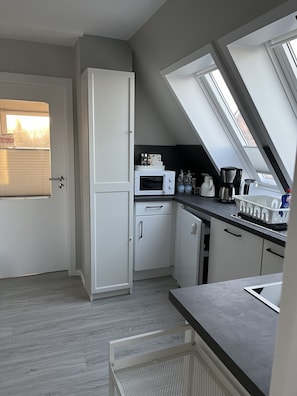 Eine kompakte Küche mit Mikrowelle, Kaffeemaschine und einem kleinen Kühlschrank. Dachfenster sorgen für natürliches Licht.