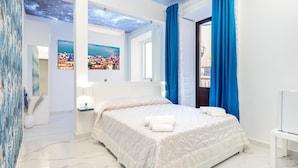 A modern bedroom with a bed, a nightstand, a mirror, and a view of a cityscape through a window. - Palazzo Bellini (Catania)