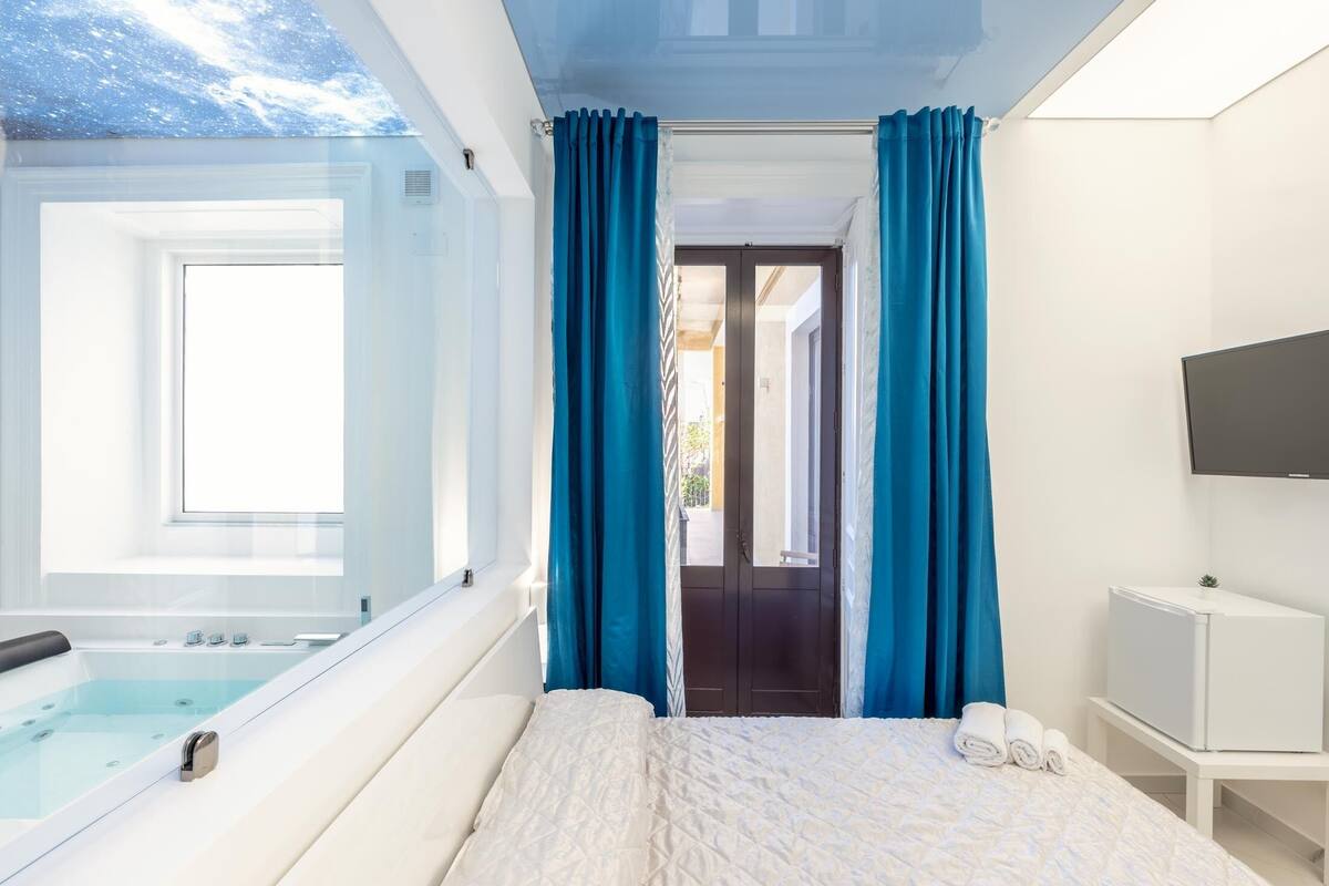 A modern bedroom with a large bed, a built-in bathtub, and a TV.