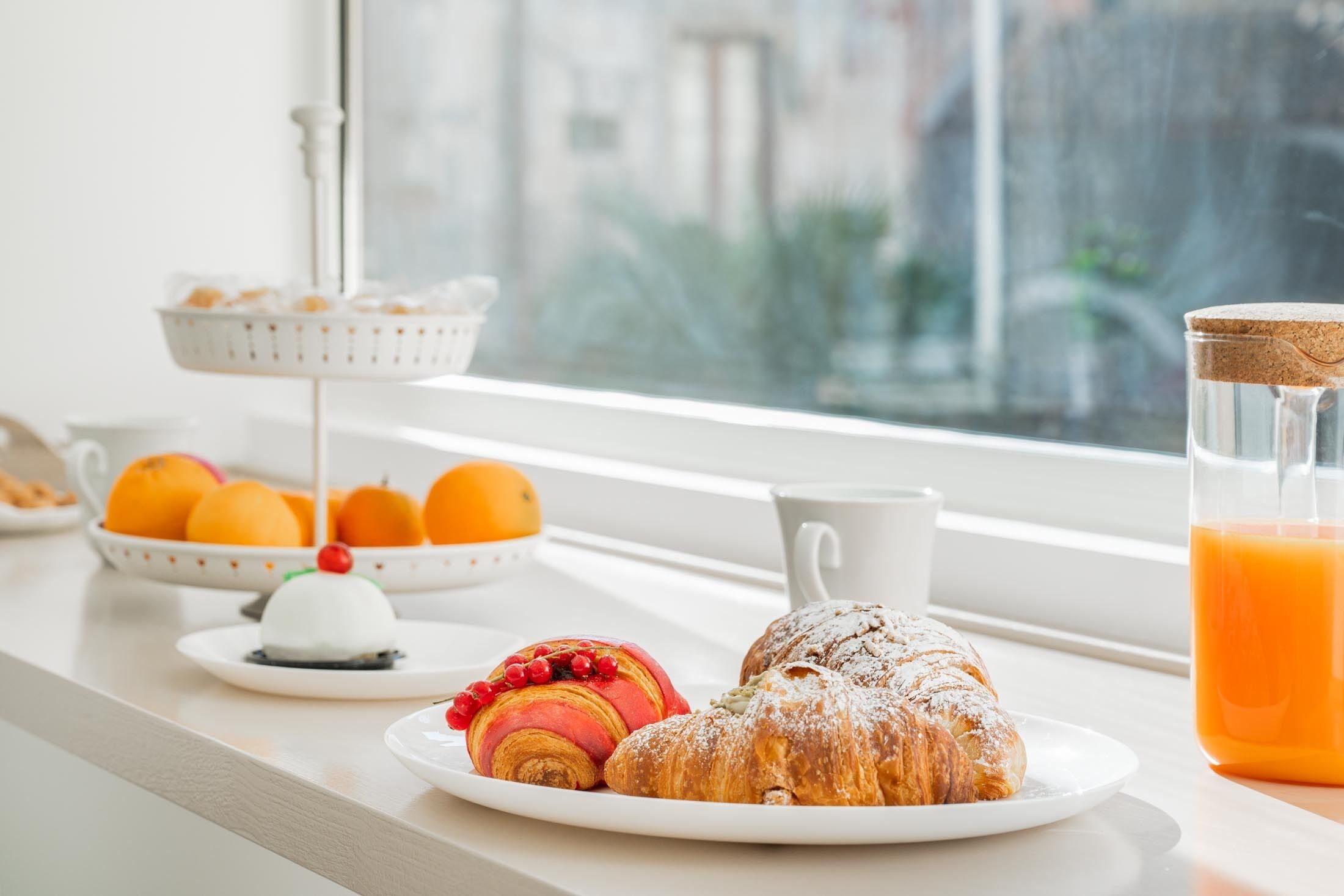 A breakfast setting with pastries and oranges on a table by a window.
