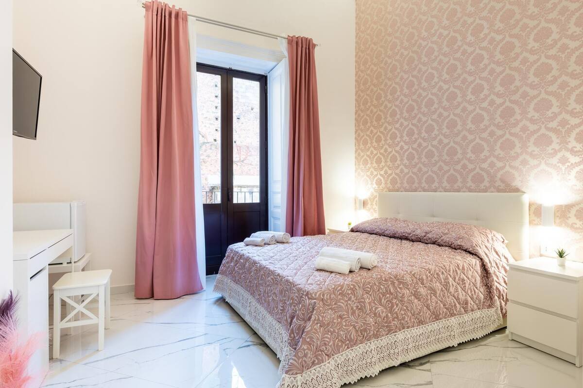 A bedroom with a bed, a desk, a chair, and a window with curtains.