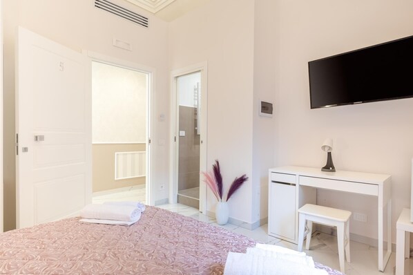 A bedroom with a bed, a desk, a TV, and a bathroom door.