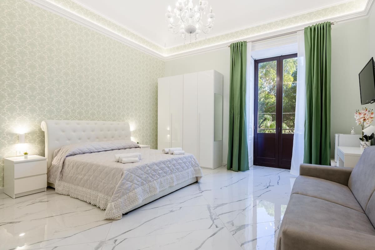 A bedroom with a large bed, a nightstand, a dresser, and a TV on the wall.