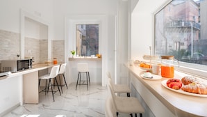 A modern kitchen with a marble floor, white cabinetry, and a breakfast setup with pastries and orange juice. - Palazzo Bellini (Catania)