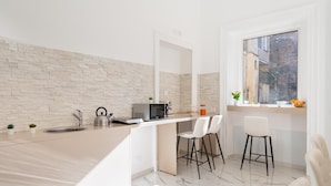 A modern kitchen with a stone backsplash, a built-in microwave, a kettle, and a window with a view of buildings. - Palazzo Bellini (Catania)