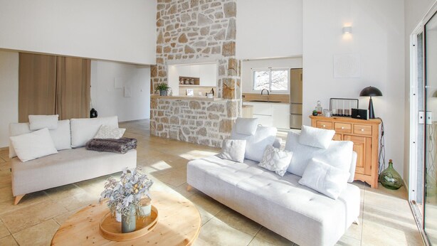 Un salon spacieux agrémenté d’un mur en pierre, un coin cuisine et un meuble en bois surmonté d’une lampe.