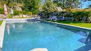 Une piscine rectangulaire à l’eau d’un bleu cristallin, entourée d’un mur de pierre et d’une pelouse agrémentée de chaises longues.
