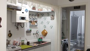 Una cocina compacta con estufa a gas, lavamanos y lavadora. Hay elementos decorativos y un mueble pequeño sobre el lavamanos.