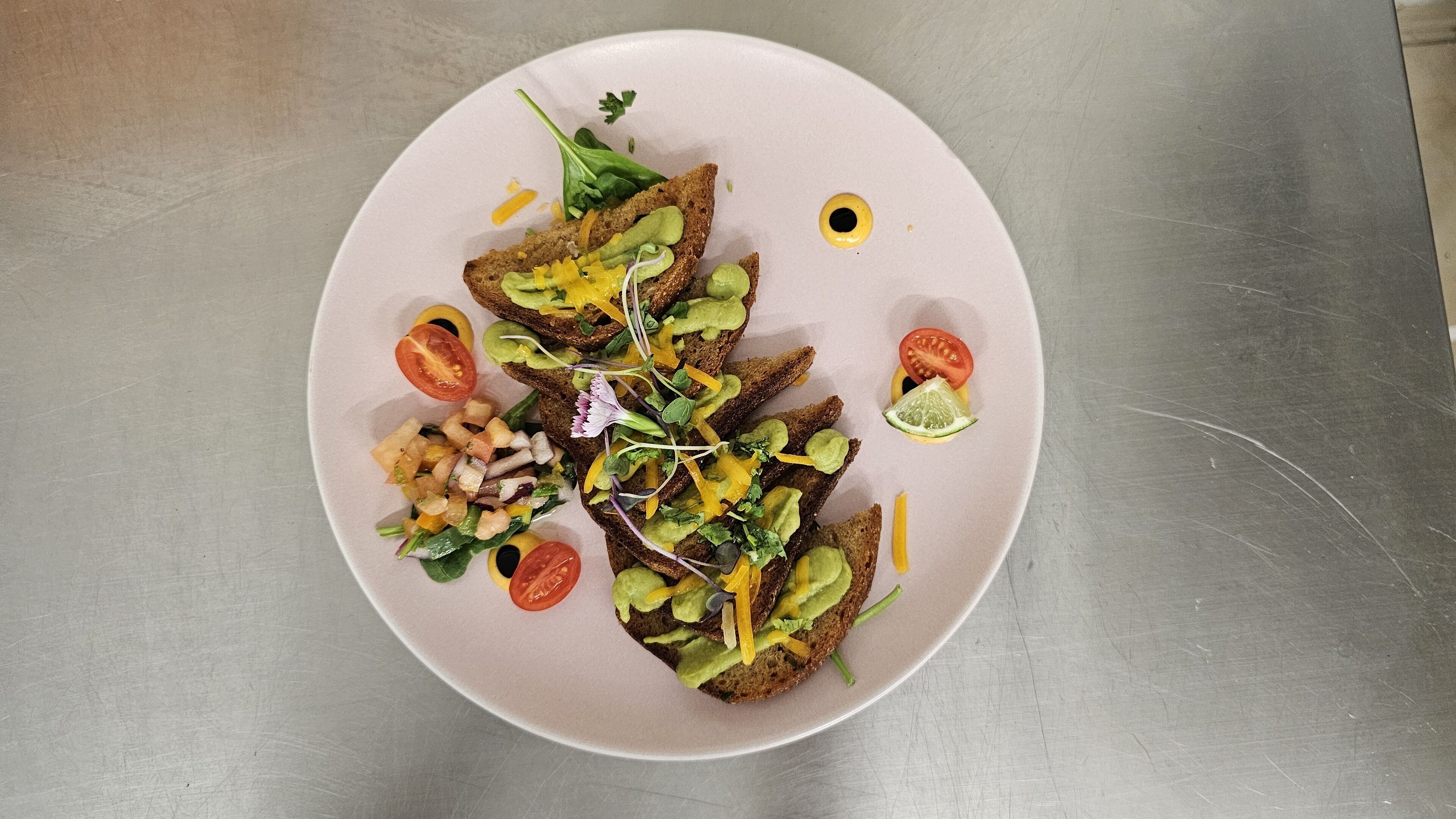 A plate with toasted bread topped with avocado, tomato, and greens, and a side salad.