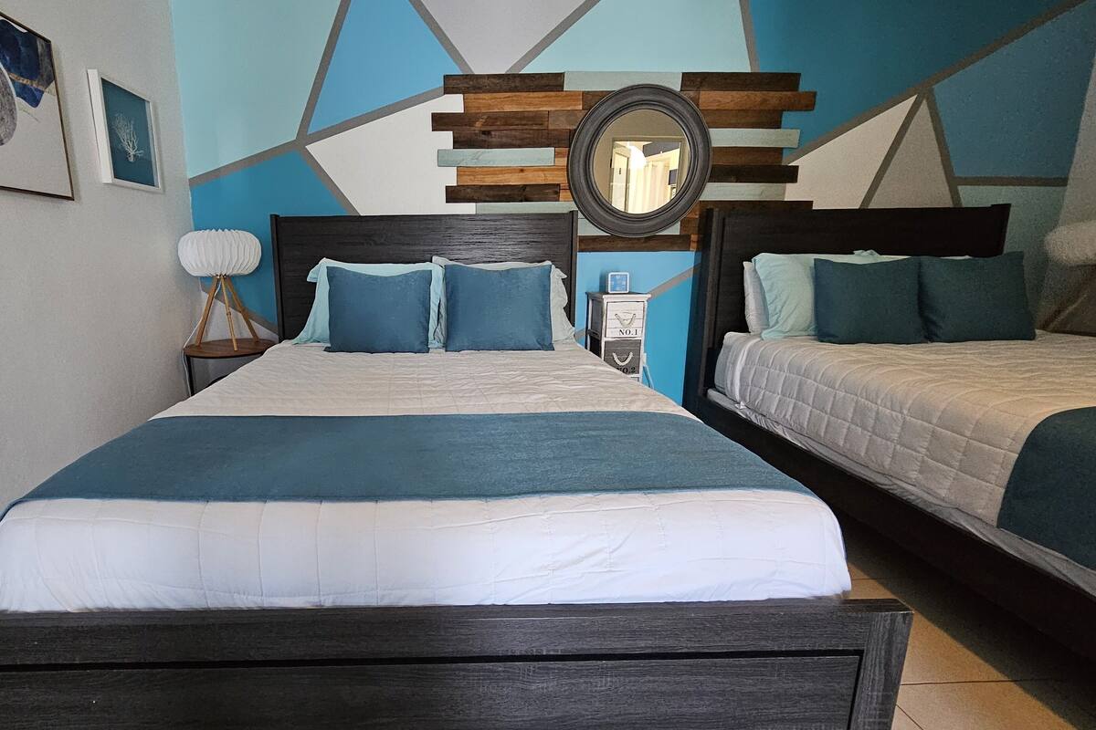 A bedroom with a large bed, two bedside tables, a nightstand, a mirror, and a wall with geometric patterns.