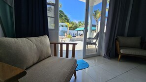 A room with a sofa, a chair, and a view of an outdoor pool area with umbrellas and chairs. - Aqua Marina Beach Club  (Rincon)