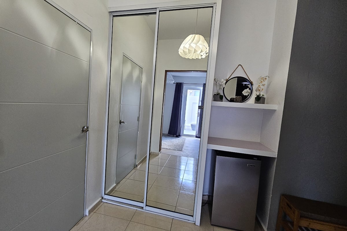A hallway with a sliding glass door leading to a room, a small refrigerator, and a shelf with decorative items.