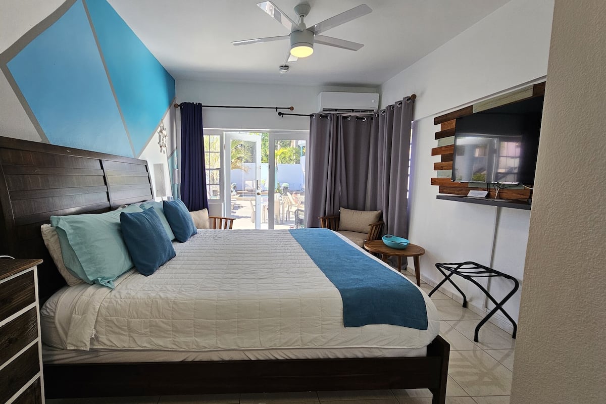 A bedroom with a bed, a desk, a chair, a TV, and a ceiling fan.