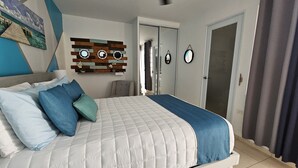 Un dormitorio con cama, almohadas, un espejo montado en la pared y una puerta.