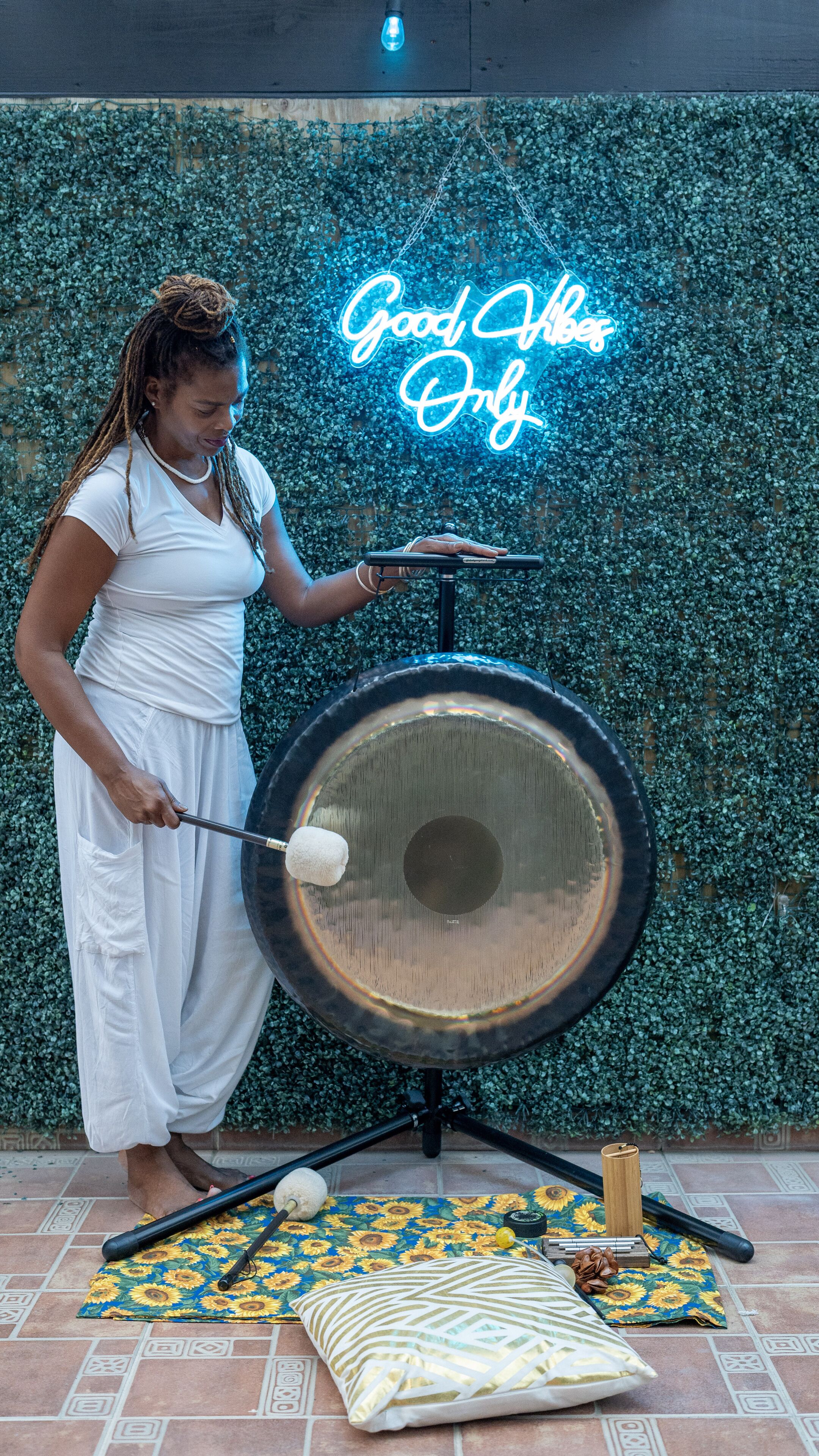 A person playing a large drum outdoors with a neon sign in the background.