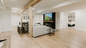 Un vaste espace de vie comprenant un canapé blanc, des poutres en bois, un téléviseur à écran plat et un coin repas avec une table et des chaises.