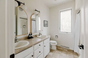 Une salle de bain avec deux lavabos, des toilettes et une fenêtre.