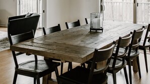 Un espace repas avec une table et des chaises en bois, un luminaire suspendu et une vue sur l’extérieur grâce à de grandes fenêtres.