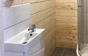 Kylpyhuone, jossa on valkoinen pesuallas, puupaneloidut seinät ja lasinen suihkukaappi.