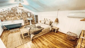Un dormitorio con pared de piedra, bañera, suelo de madera y cama con almohadas.